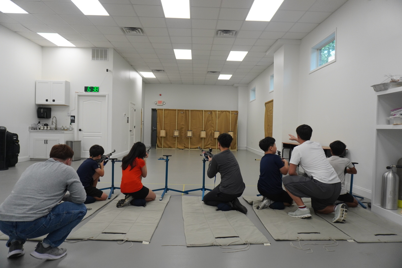 Coach guiding young athletes during kneeling air rifle practice